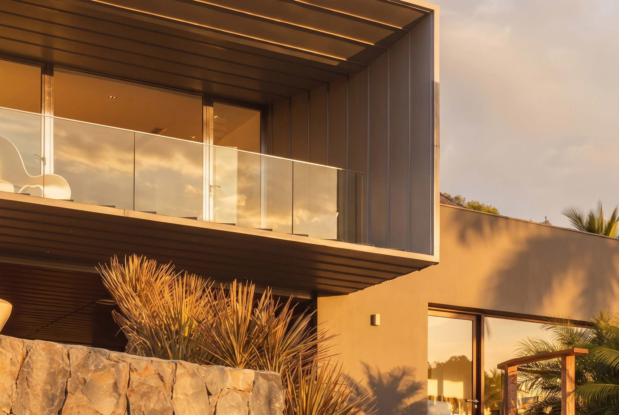 The house at golden hour: zinc cladding, glass balustrade and the stone wall below